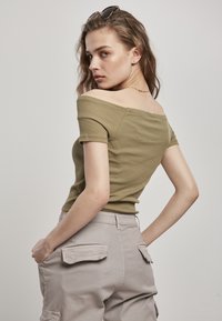 Top de canalé verde oliva con escote asimétrico, combinado con pantalones cargo de un gris claro, que cuentan con bolsillos laterales y una silueta ajustada.