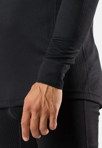 Schwarz, geripptes Langarmoberteil mit taillierter Passform. Verfügt über einen Rundhalsausschnitt und Bündchenärmel. Das Material wirkt dehnbar und glatt.