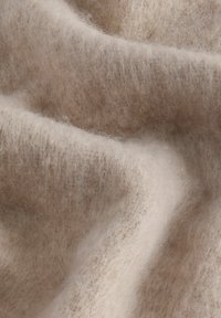 Tissu en laine beige clair avec une texture douce et duveteuse, présentant de légères ondulations et une apparence lisse et chaleureuse.