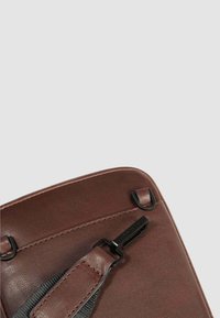 Borsa in pelle marrone con una texture liscia, dotata di accessori neri e una tracolla regolabile, che mostra dettagli di cucitura e bordi arrotondati.