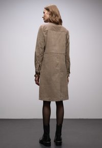 Vestito in lino beige con maniche lunghe, taglio dritto e dettaglio con cucitura posteriore. Indossato con stivaletti neri e calze trasparenti.