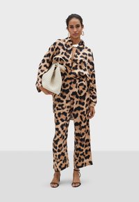 Ensemble assorti en imprimé léopard avec une chemise décontractée et un pantalon large, en tissu lisse. Un sac seau tissé blanc cassé complète le look.