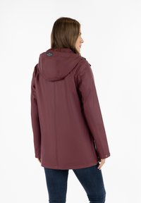 Vandafvisende bordeaux jakke med hætte, glat tekstur, lange ærmer og lige skæring. Har et logo mærke på bagsiden.