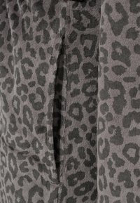 Grå stof med en struktureret kordfløjlsoverflade, der har et sort leopardprintmønster. Inkluderer en sidelomme, der er synlig i designet.