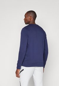 Marineblaue Langarm-Sweatshirt, Baumwollmischung, Rundhalsausschnitt, gerippte Bündchen, glatte Textur, schlichtes Design, getragen mit weißen Hosen.