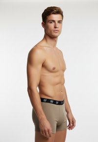 Beige boxer briefs with a black CR7 waistband, featuring a snug fit and smooth texture. Model shown from the side against a white background.
