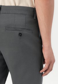 Graue Hose mit glatter Textur, ausgestattet mit einer Gesäßtasche, die durch einen schwarzen Knopf gesichert ist, und einem maßgeschneiderten Schnitt.
