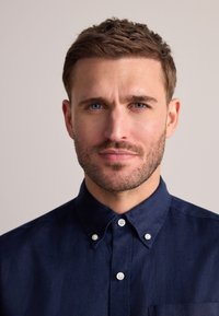 Camicia blu navy con bottoni e colletto, realizzata in tessuto strutturato. La camicia presenta bottoni bianchi e una tasca semplice sul lato sinistro.