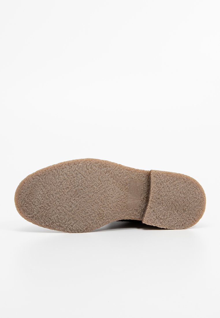 Braune Gummisohle mit strukturierten Grip-Mustern. Abgerundete Form und flacher Absatz. Leicht geprägtes Logo nahe dem Absatz.