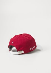 Rød bomull baseballcaps med hvit skjerm, med et lite flagg emblem og hvit brosjert signatur bak. Justerbar stropp.