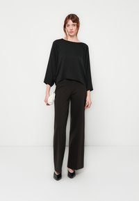 Svart oversized topp med båthals, parret med vide mørkebrune bukser. Fullført med en liten hvit håndveske og svarte hæler.