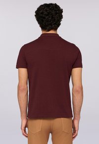 Bordový polo tričko s krátkým rukávem a klasickým límečkem, s rovnými lemy a diskrétními švy na zadní straně.