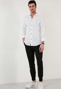 Witte linnen shirt met zwarte knopen en een borstzak, gecombineerd met zwarte taps toelopende joggers en witte sneakers. Eenvoudig en modern ontwerp.