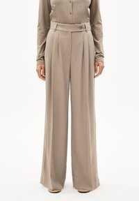 Weite Hosen aus hellbeigem Stoff. Mit hoher Taille, Falten und einem Knopfdetail vorne. Glatte Textur mit klaren Linien.