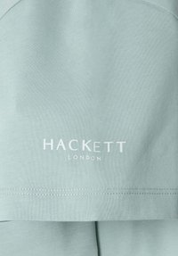 Svetlozelená bavlnená tkanina so viditeľnou rebrovou textúrou; obsahuje biele logo "HACKETT LONDON"; rovný lem s úhľadným šitím.