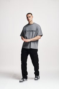 Tricou supradimensionat gri cu textul "ZY STUDIOS" în negru, asortat cu pantaloni cargo negri și adidași alb-negru. Textură de stofă netedă.