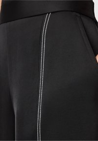 Close-up van zwarte broek met zijzak en verticale dubbele witte stiksels.