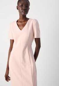Pink short-sleeve dress with a V-neck, tailored fit, and structured seams. Made from smooth fabric, features subtle vertical lines.