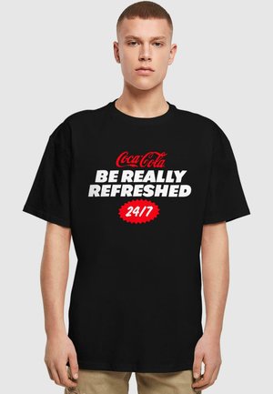 Black cotton t-shirt featuring large white text "BE REALLY REFRESHED" and red Coca-Cola logo, with a round red accent stating "24/7."