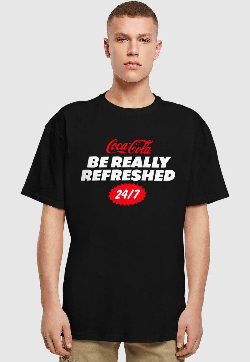 Black cotton t-shirt featuring large white text "BE REALLY REFRESHED" and red Coca-Cola logo, with a round red accent stating "24/7."