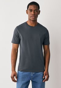 Grijs T-shirt met ronde hals van glad katoen. Korte mouwen, slim fit, met een klein logo op de linkerborst. Gecombineerd met een blauwe spijkerbroek.