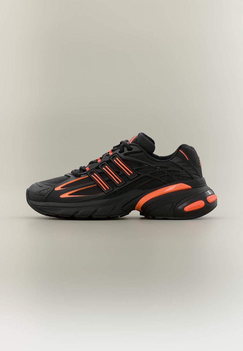 Chaussure de sport noire avec des accents orange, tige en mesh et synthétique, semelle épaisse avec talon amorti, et lacets pour la fermeture, vue latérale.