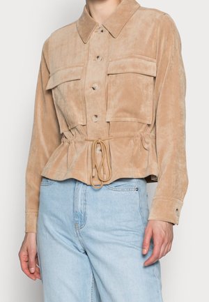 Beige kordjakke med knapper, store frontlommer og snøre i taljen, båret med lyseblå denimjeans.