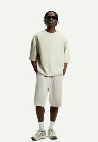 Light beige oversized short-sleeve shirt and matching shorts. Features a relaxed fit, minimal stitching details, and paired with beige sneakers.
