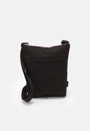 Sac bandoulière noir en toile avec zip, design plat, sangle ajustable et petite poche avant. Tissu texturé avec des détails minimalistes.