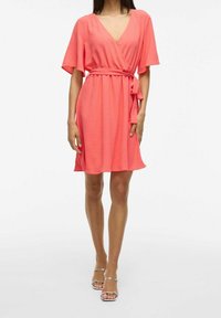 Korálové zavinovací šaty s krátkými kimono rukávy, strukturovanou látkou, páskem v pase a sukní do poloviny kolen. Nosit se stříbrnými sandály na pásky.