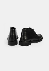 Bottines en cuir noir avec un bout rond, une texture lisse, des talons blocs bas et un design minimal de laçage. Aucune motif ou accent visible.