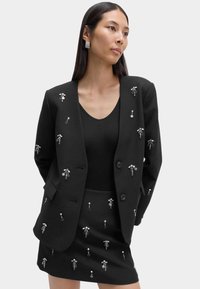 Schwarzes Blazer- und Minirock-Set mit silbernen Verzierungen, strukturiertem Design und glattem Stoff. Knöpfe am Blazer.