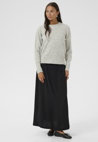 Lichtgrijze wollen trui met een ronde hals, gecombineerd met een zwarte maxirok. De outfit heeft lange mouwen en een relaxed fit.
