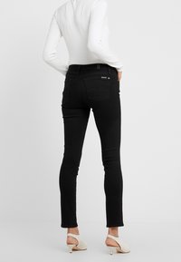 Svarta slim fit jeans med en slät yta, midja som sitter mitt emellan, och två bakfickor. Kombineras med ljusa, låga skor.