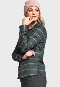 Tmavě zelená košile s dlouhým rukávem, šedými horizontálními pruhy, zapínací límec, postranní rozparky a vyšívané logo na rukávu. V kombinaci s růžovou pletenou čepicí.