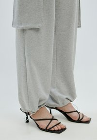 Grijze, lichte, opgeschorte sweatpants gecombineerd met zwarte strappy hakken met een vierkante neus en dunne banden.