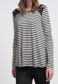 Svartvitt randig långärmad topp med lös passform, med spetsdetaljer på axlarna och sidoflikar för ökad rörelsefrihet.