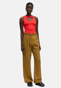 Rotes ärmelloses Top mit Ausschnitt, kombiniert mit hoch taillierten, weit geschnittenen Senfgelb-Hosen und flachen schwarzen Sandalen. Glatte Texturen und minimalistisches Design.