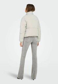 Lichtgrijze pufferjas met een hoge kraag, kort ontwerp en elastische manchetten, gecombineerd met grijze uitlopende jeans en zwarte hakken.