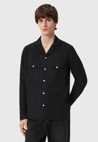 Sort langærmet skjorte med broderet blomstermotiv på kraven, to brystlommer og sølvfarvede firkantede knapper. Blødt stof.