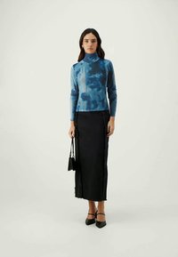 Blue tie-dye long-sleeve top with a high neck, paired with a black fitted midi skirt featuring a textured side seam and subtle fraying.