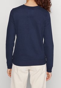 Sweat-shirt bleu marine avec un col ras du cou, des manches longues, des poignets et un bas côtelés, fabriqué en tissu lisse, vu de dos.