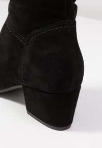 Stivale alla caviglia in suede nero con una finitura testurizzata, caratterizzato da un tacco robusto e dettagli di cucitura puliti. Design semplice e minimalista.