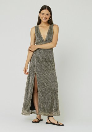 Robe maxi sans manches noire et dorée avec un décolleté en V profond, une fente à l'avant et un motif texturé. Associée à des sandales plates noires.