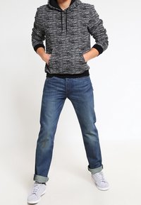 Svart och vit melerad hoodie med en ficka fram och dragsko. Blå denimjeans med uppvikt benslut. Vita sneakers med svarta detaljer.