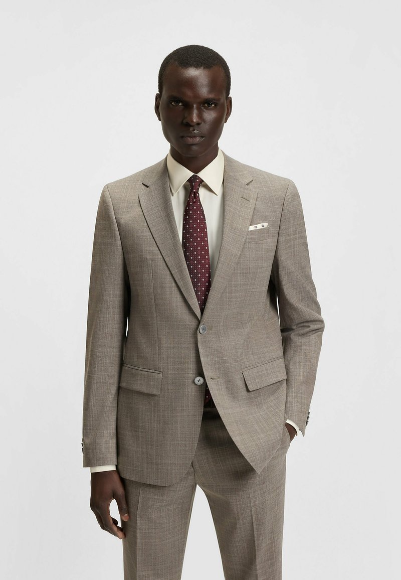 Beige checkered suit with a fitted design, featuring two front pockets, and a maroon polka dot tie. White shirt visible underneath.