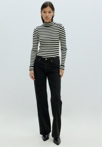 Schwarze, hoch taillierte Jeans kombiniert mit einem schwarz-weißen gestreiften Rollkragenoberteil. Das Outfit zeichnet sich durch enganliegende Ärmel und elegante Designelemente aus.