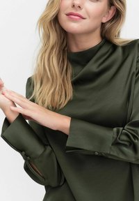 Olivi vihreä satiinipaita, jossa on korkea kaulus, pitkät hihat ja nappiyksityiskohtia hihoissa. Omistaa sileän, kiiltävän pinnan.