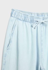 Pantalon en jean bleu clair avec taille élastique et cordon de serrage, avec poches latérales et coutures apparentes.