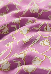 Rosa tyg med ett blommönster av vita tulpaner kantade med guld, som visar en slät textur med mjuka veck och draperingar.